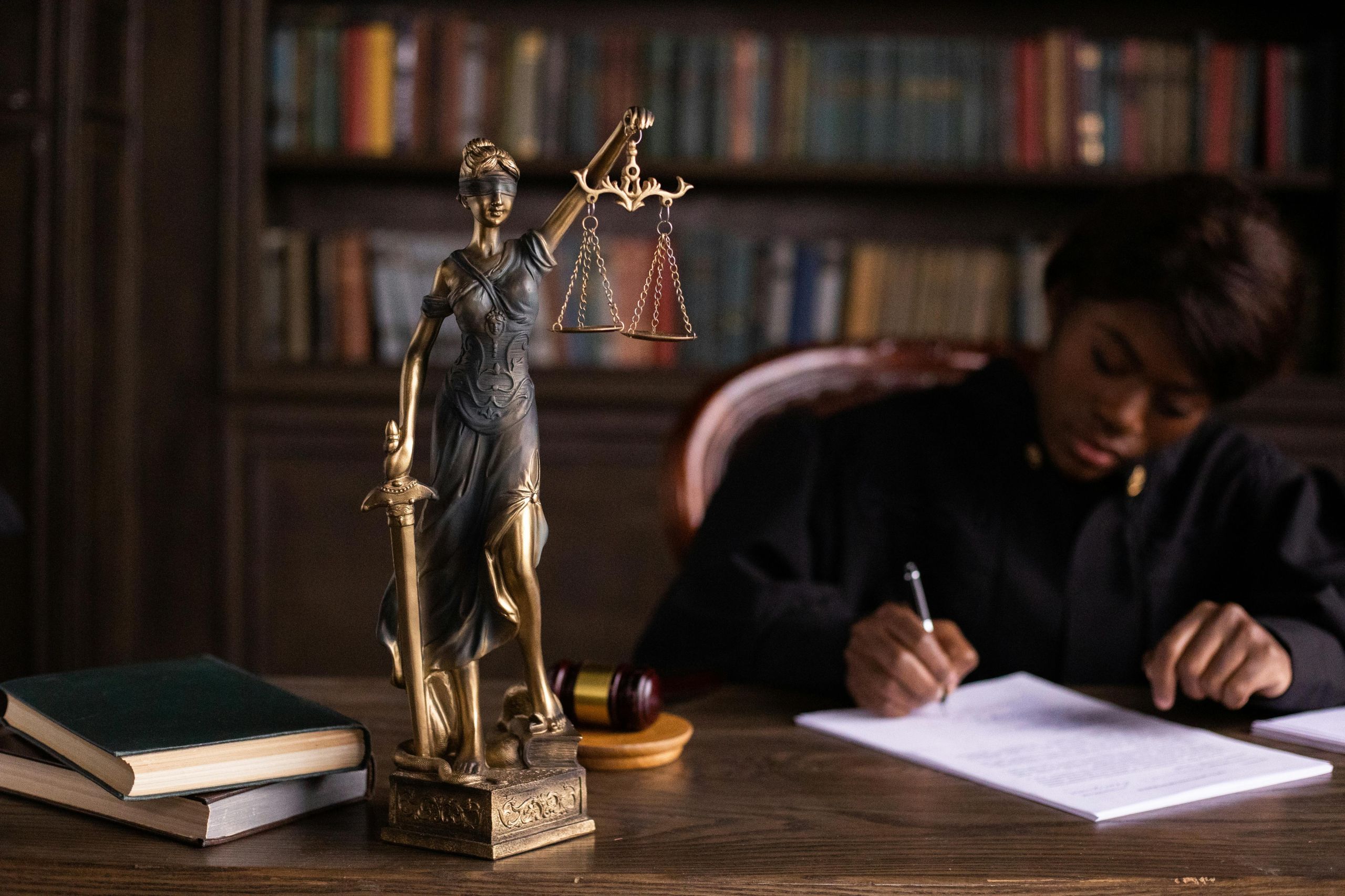 Figurine of the Lady Justice in foreground, Judge taking notes in background
