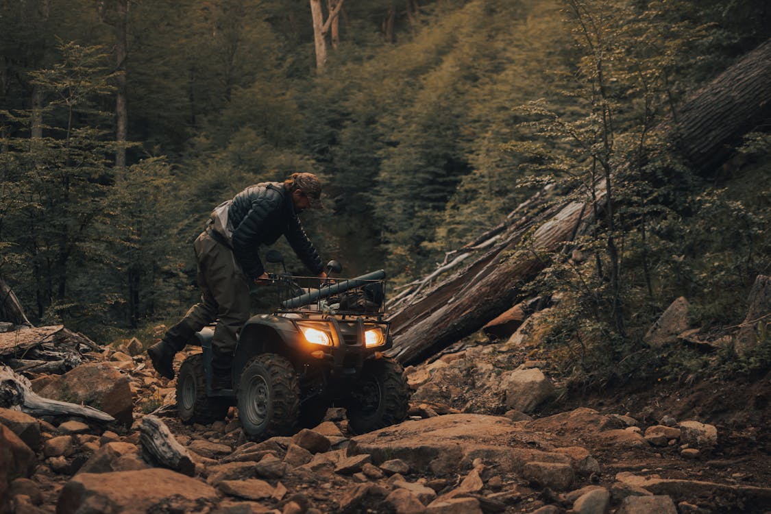 man in forest climbing aboard his all terrain vehicle