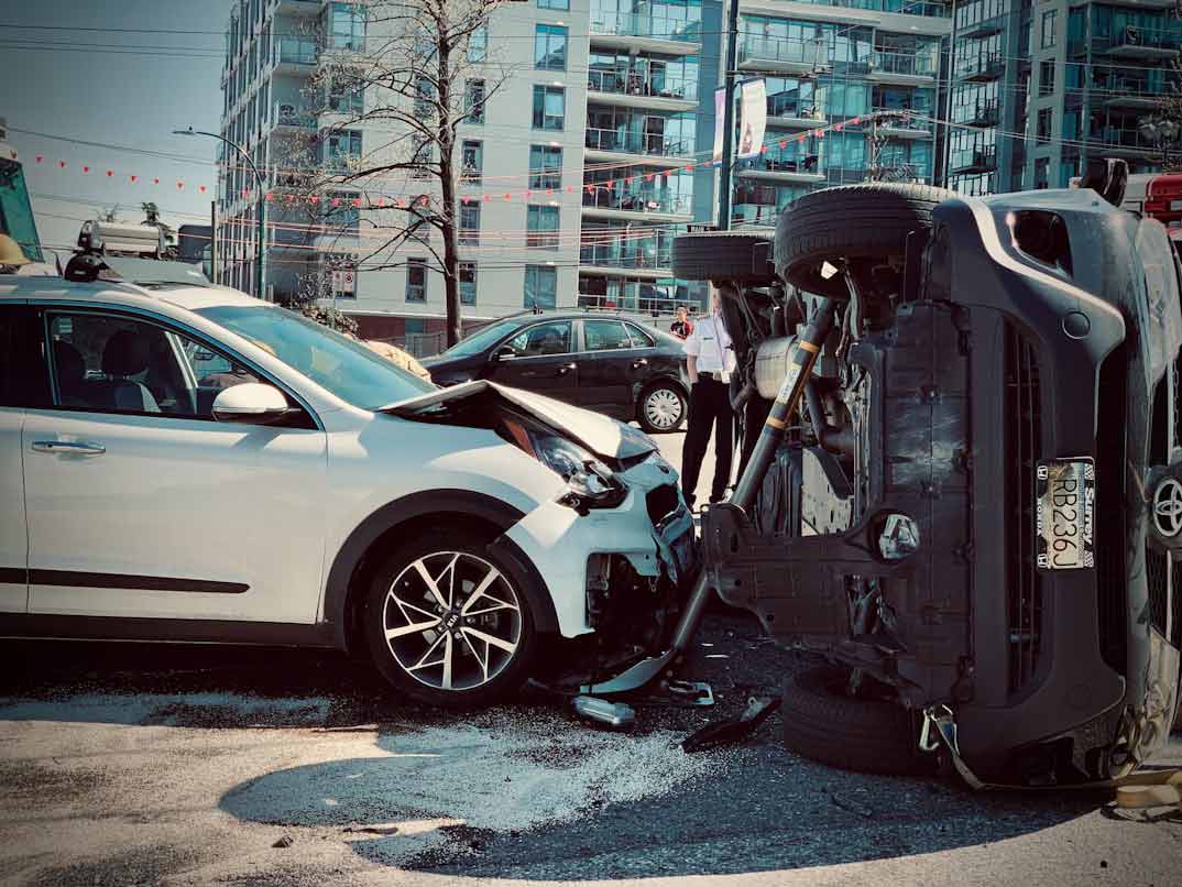 A picture of a white car crashed into another car that is flipped onto its side