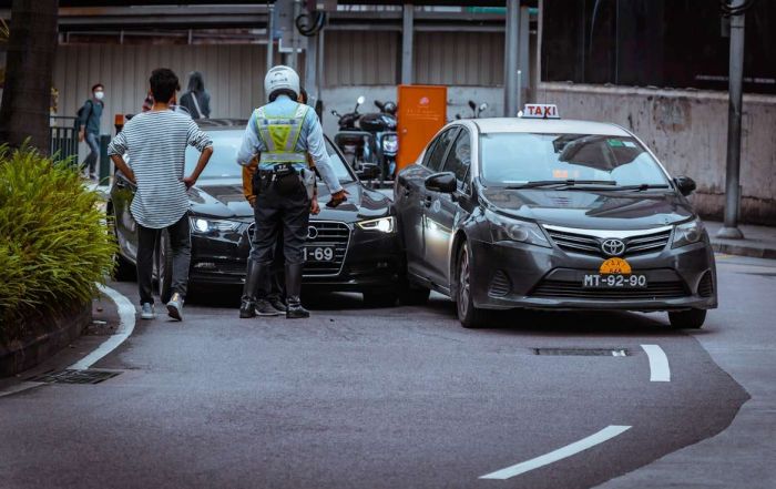 A police officer and civilian standing at the scene of two cars in a car accident