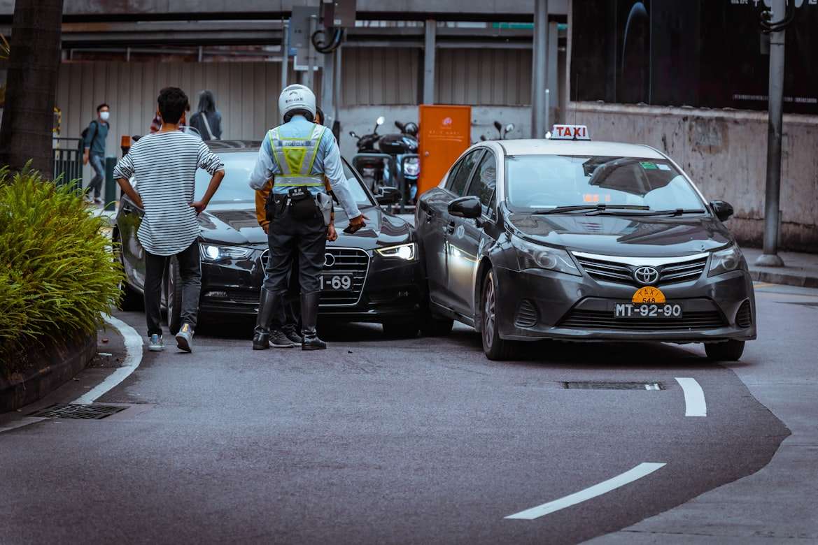A police officer and civilian standing at the scene of two cars in a car accident