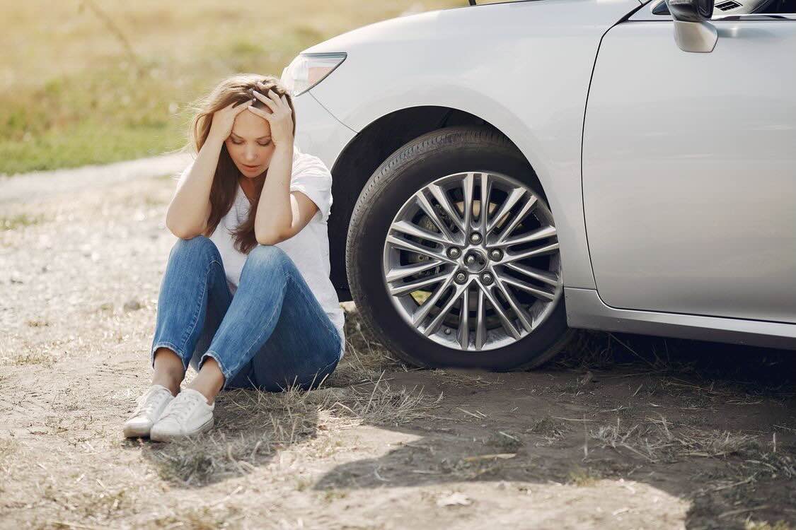 A woman looking upset, sitting outside of her car